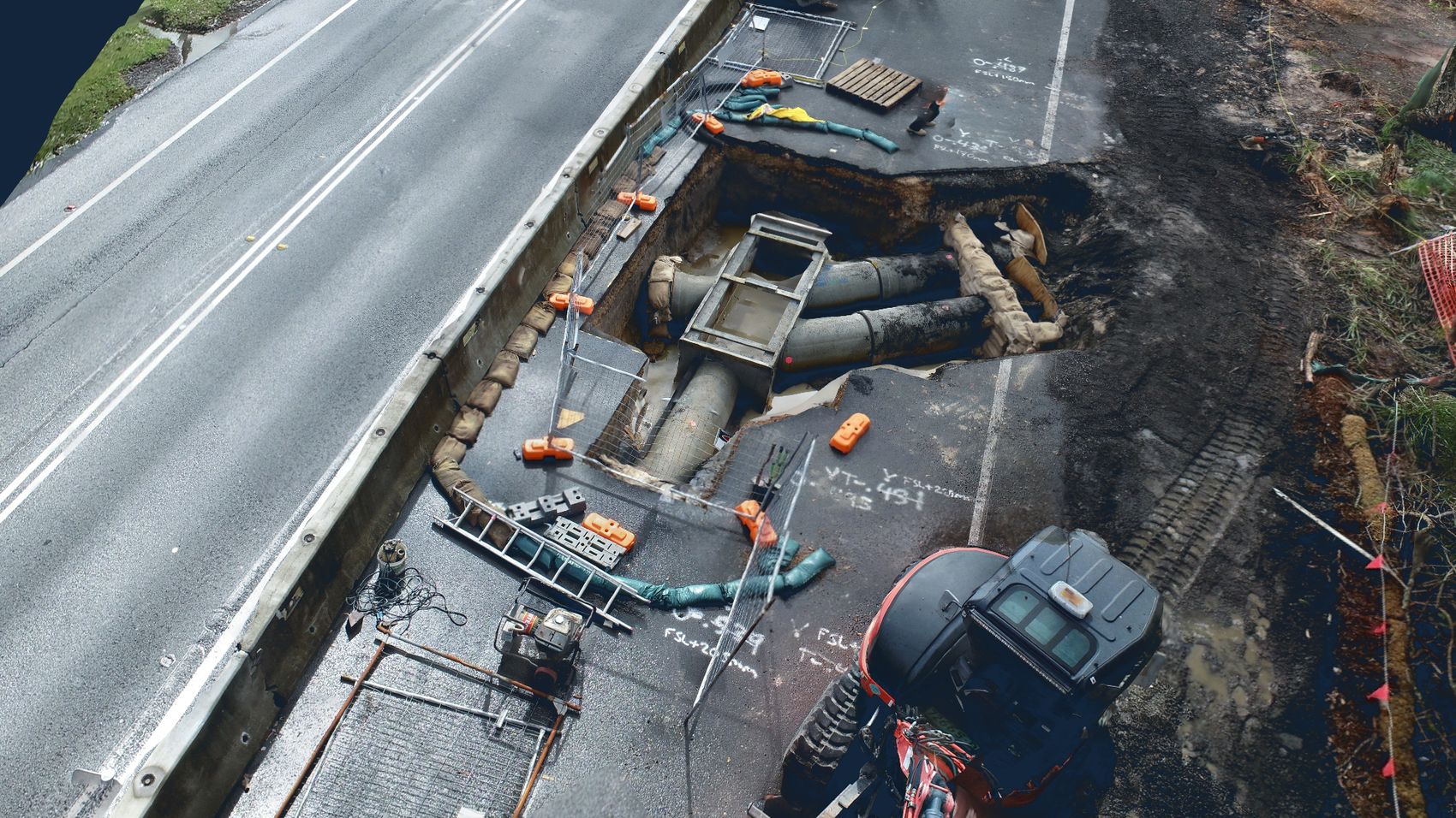 Drone model of a stormwater excavation beneath a road shoulder, showing exposed pipework, pit and shoring alongside live traffic lanes
