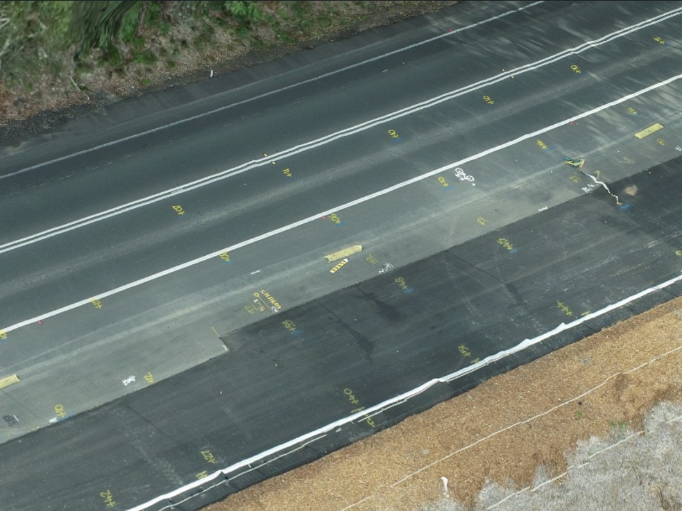 Freshly paved asphalt lanes with survey markings and chainage set out across the mat