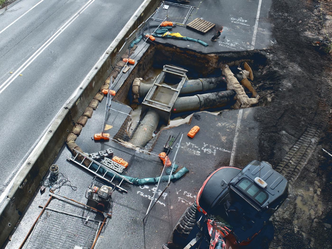 Stormwater pit and pipework exposed in an excavation beside a guardrail